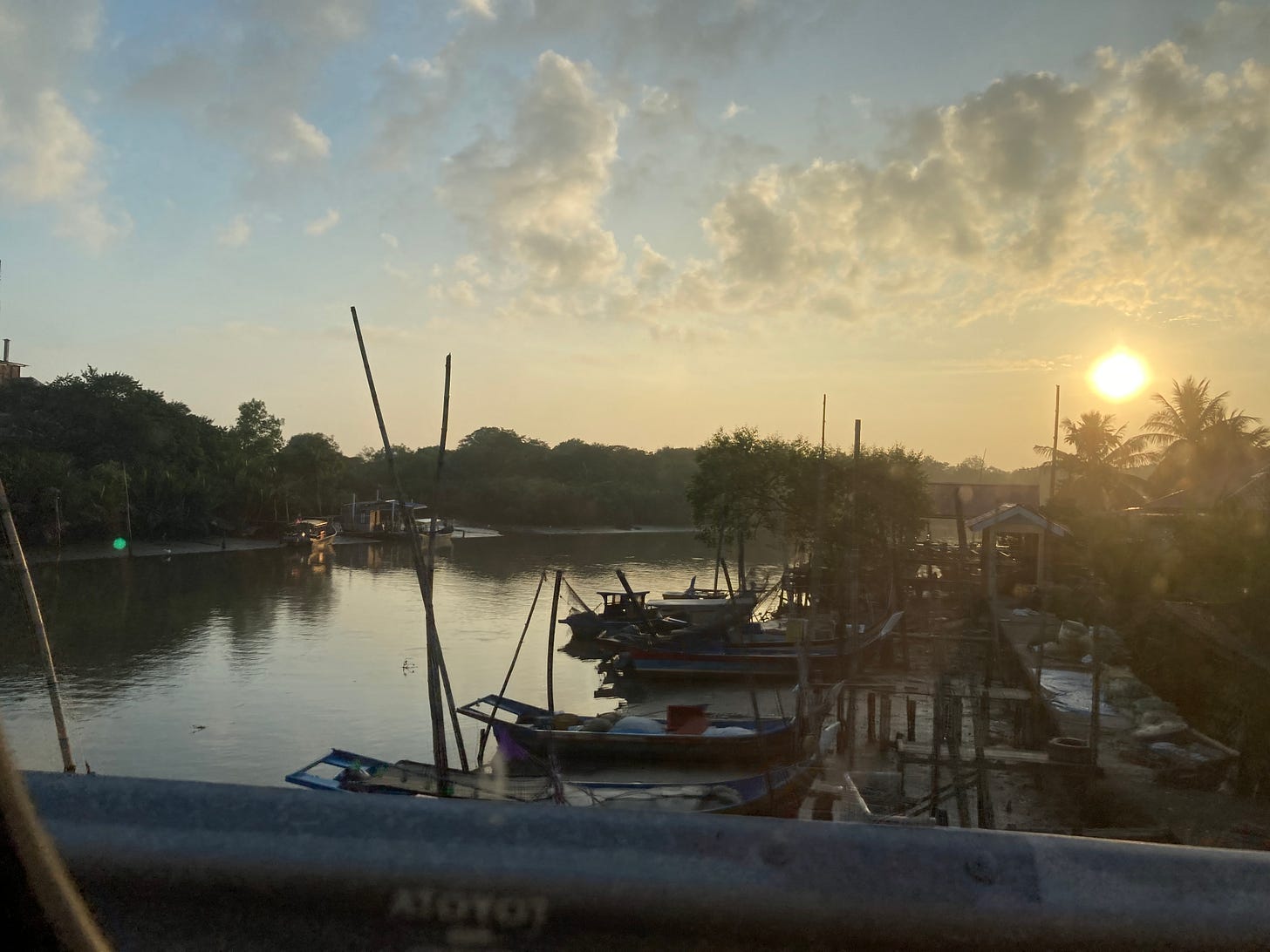 a photo taken through a grimy car window of a sun rising over a fishing village, boats moored at the edge