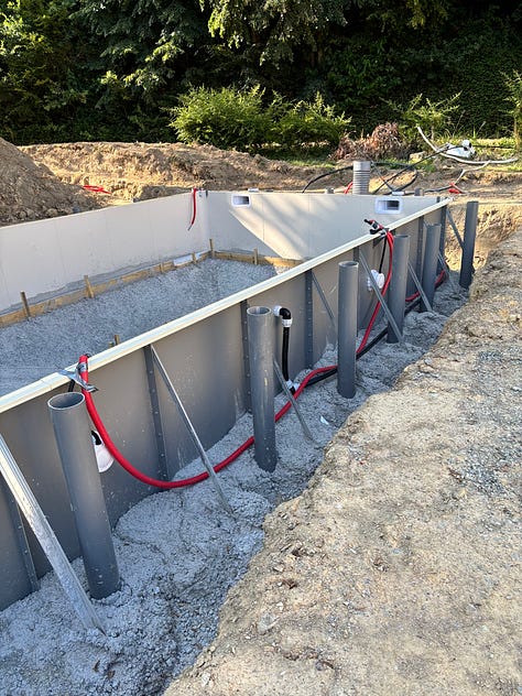 Pool construction at the château, with a concrete truck pouring beside the towers, a pool shell with pipes, and a trench of electrical cable;