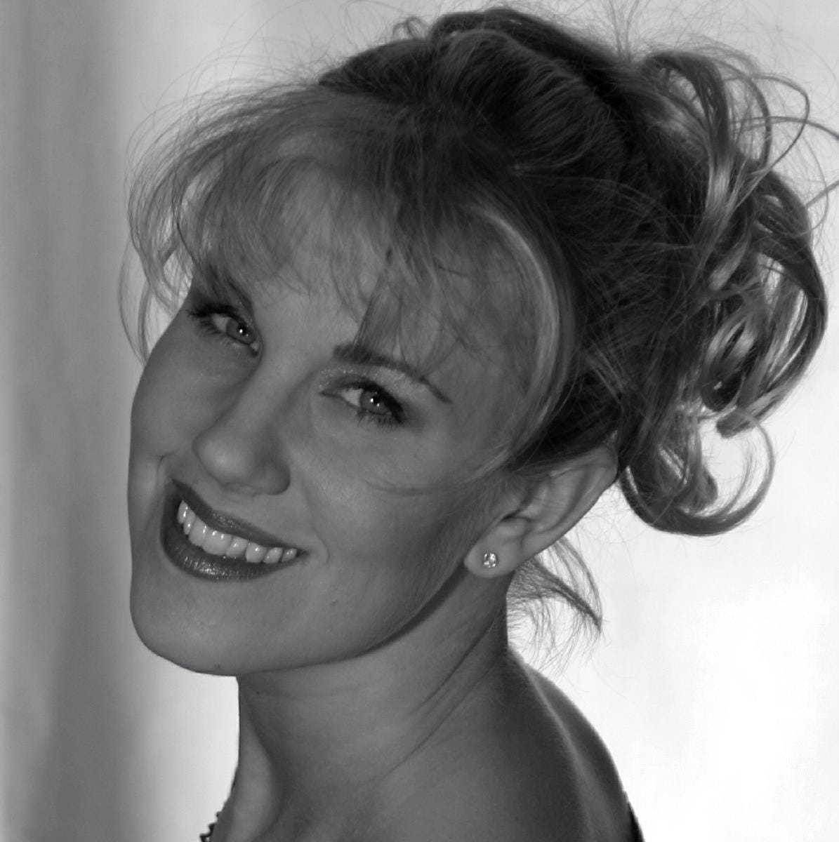 A black and white picture of Solinea, who is about as classically gorgeous as it gets. In this headshot, she's looking back over her shoulder and smiling, her makeup perfect, her blonde hair messy but in a beautiful way. Not the way my hair is messy, which is in a "When was the last time I took a shower?" kind of way.