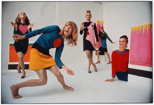5 femmes en robes et jupes colorées, avec des motifs genre gros cœur rose ou grand point rouge, posent devant un fond blanc en souriant et en se déhanchant.