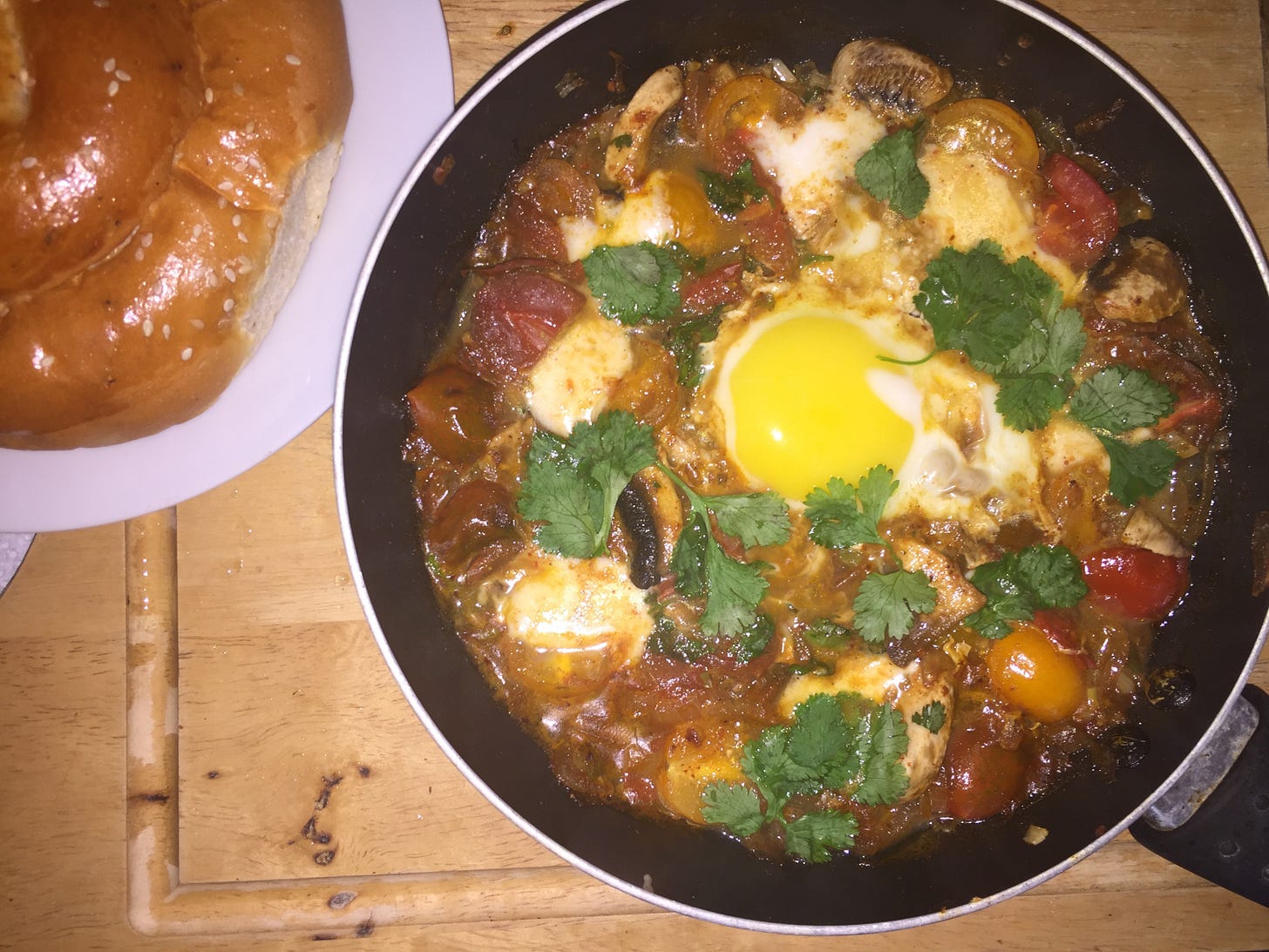 Shakshuka with colorful cherry tomatoes, mushrooms, mozzarella, and cilantro, topped with an egg and served with challah bread. Part of Liat Portal’s Foodie Disorder journey on The Liat Show.