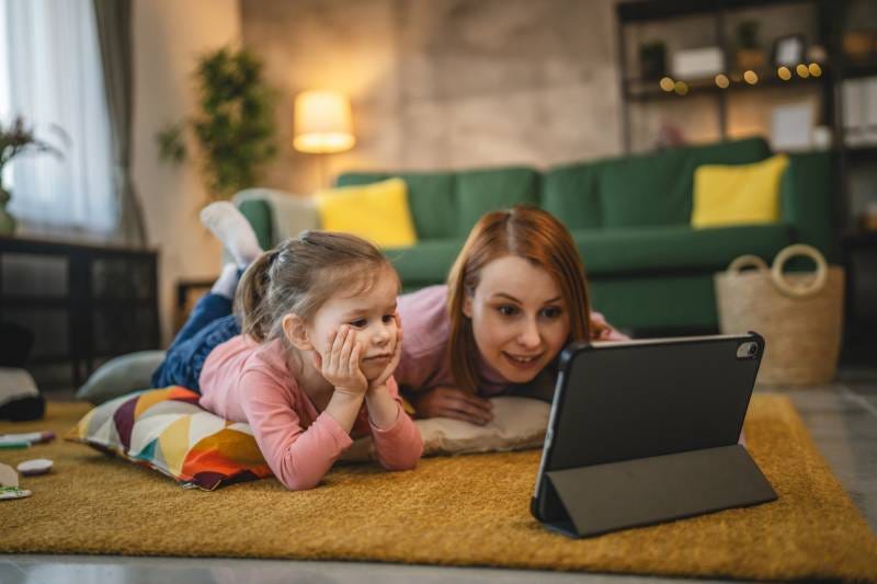 Mother and daughter use digital tablet to on living room floor