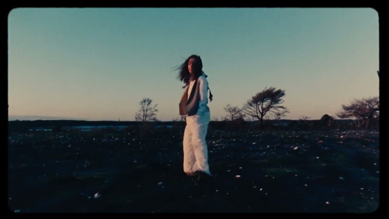 A young woman dressed in all white on a dirt field looking back to the camera. Her cuffs are dirty.