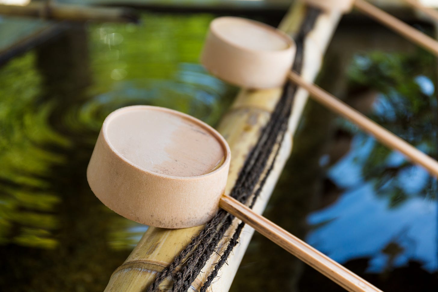Close-up of wooden water scoops resting on bamboo at a Japanese onsen, with water rippling in the background. Close-up of wooden water scoops resting on bamboo at a Japanese onsen, with water rippling in the background.