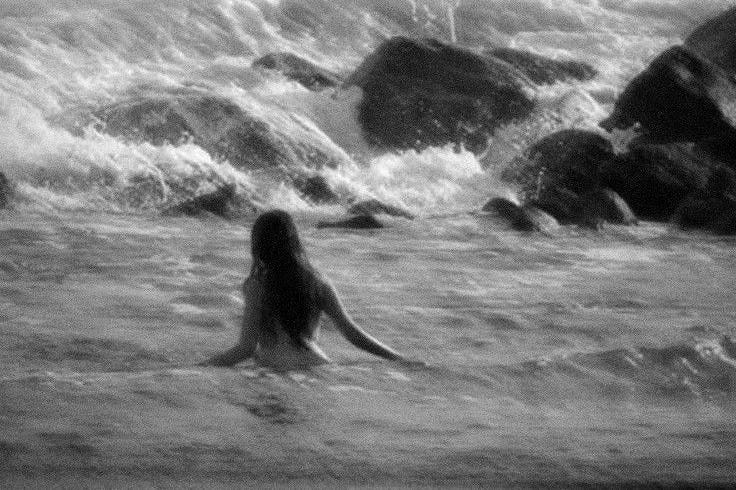 This may contain: a woman is sitting in the water near rocks This may contain: a woman is sitting in the water near rocks