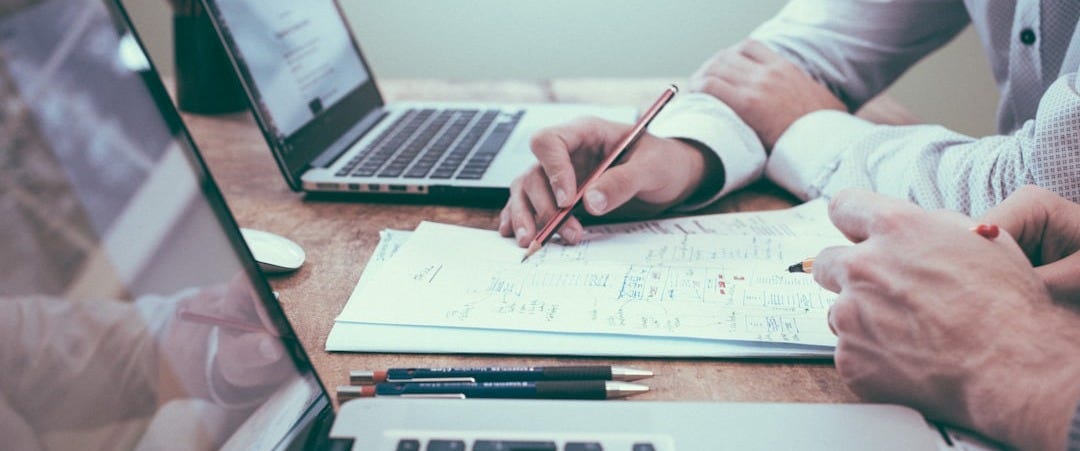 person holding pencil near laptop computer