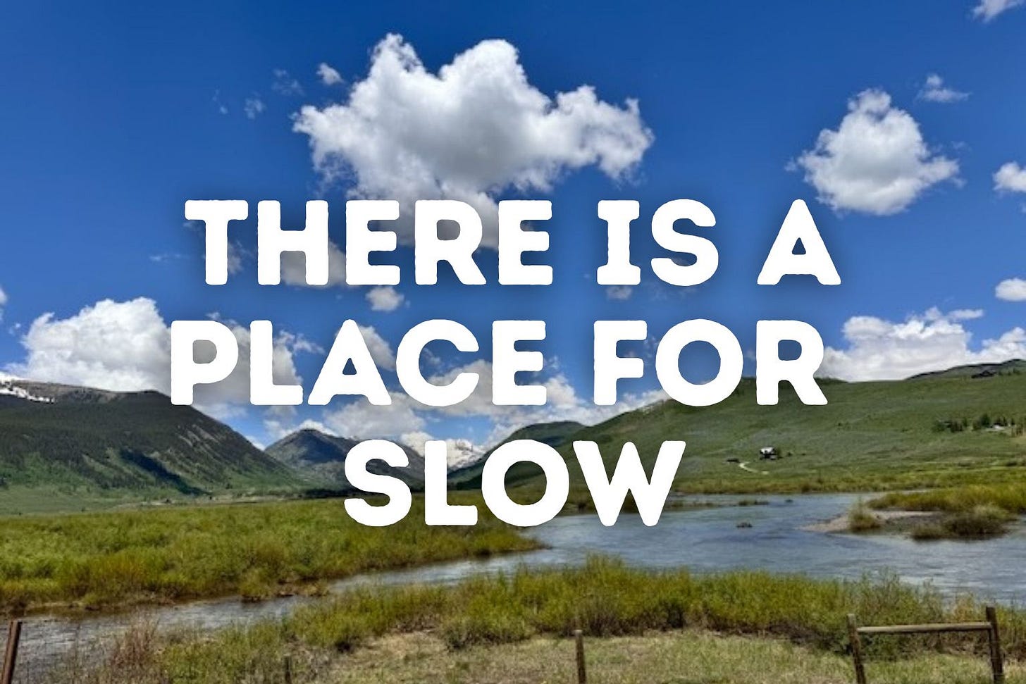 A serene mountain valley near Crested Butte, Colorado, with a slow-moving river winding through green brush under a bright blue sky filled with fluffy white clouds. Snow-capped peaks rise in the distance. Large white text is overlaid across the sky and landscape reading: “THERE IS A PLACE FOR SLOW.” The scene evokes calm, spaciousness, and an invitation to pause. A serene mountain valley near Crested Butte, Colorado, with a slow-moving river winding through green brush under a bright blue sky filled with fluffy white clouds. Snow-capped peaks rise in the distance. Large white text is overlaid across the sky and landscape reading: “THERE IS A PLACE FOR SLOW.” The scene evokes calm, spaciousness, and an invitation to pause.