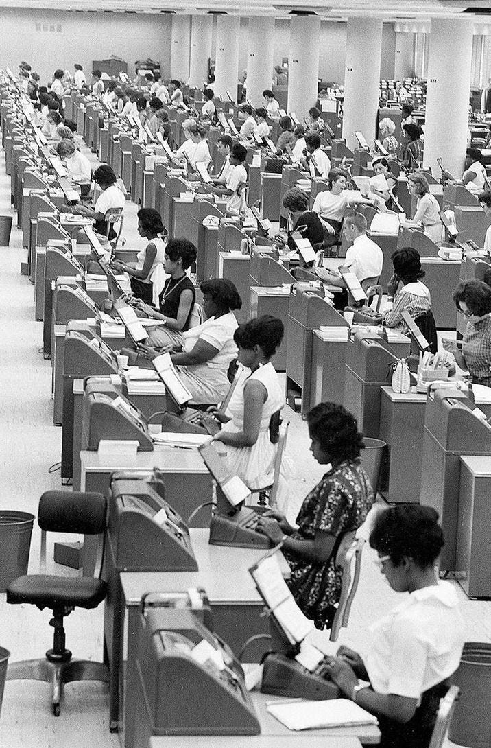 This may contain: many people are sitting at desks in an office with computers and books on them