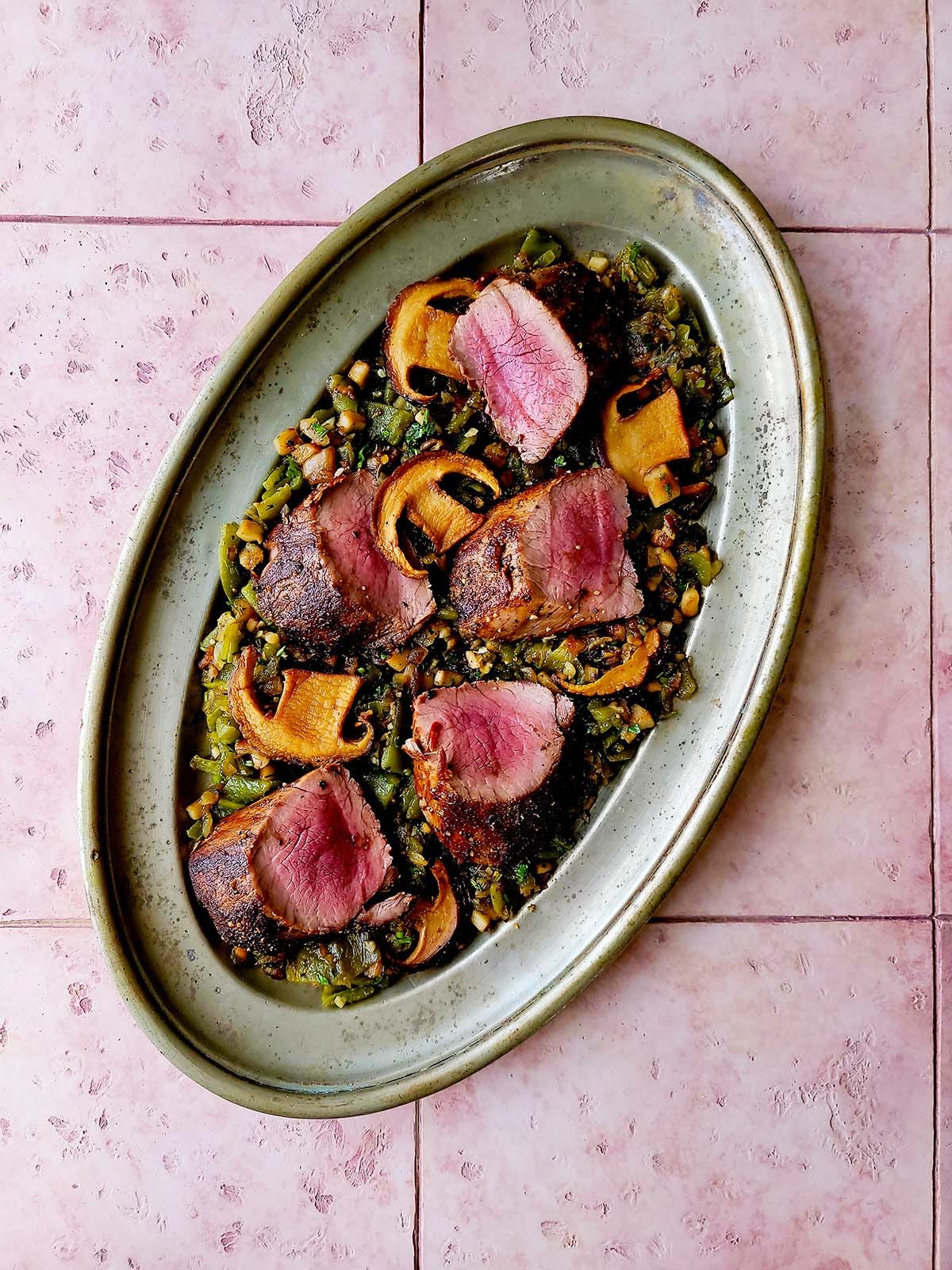 A platter of venison steak with mushrooms and green chiles. 