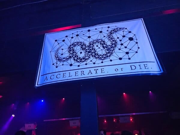 A light blue flag with a snake inside a net and the words, Accelerate or Die across the bottom.