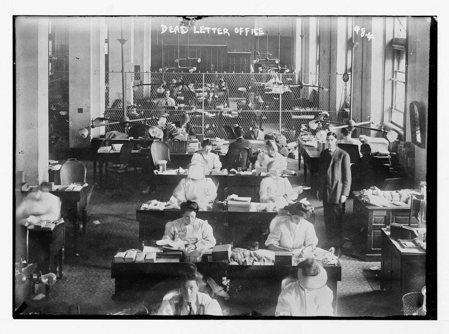 A large hall of clerks at desks heaped with opened and unopened post. A large hall of clerks at desks heaped with opened and unopened post.