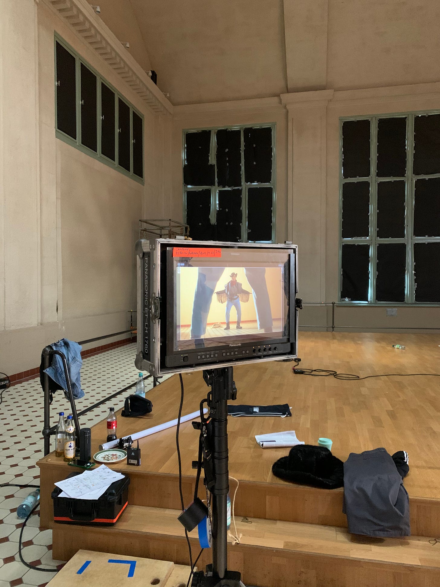 image of a monitor standing inside a big turbine hall with the window light blocked out. on the monitor is a cowboy, standing at a distance. in the foreground are an identical cowboy's legs, framing the cowboy in the background.