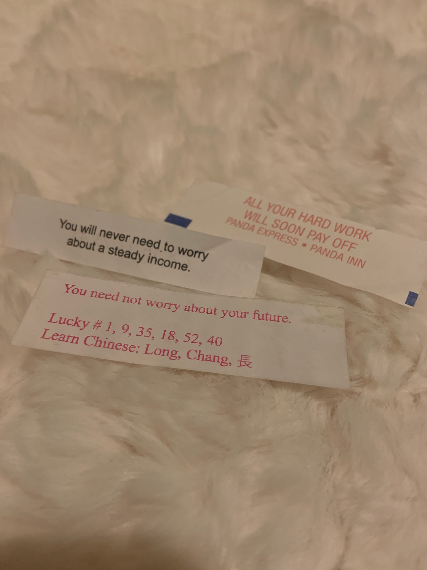 Three rectangular slips of white paper lay on top a white blanket with their text visible to the reader. 