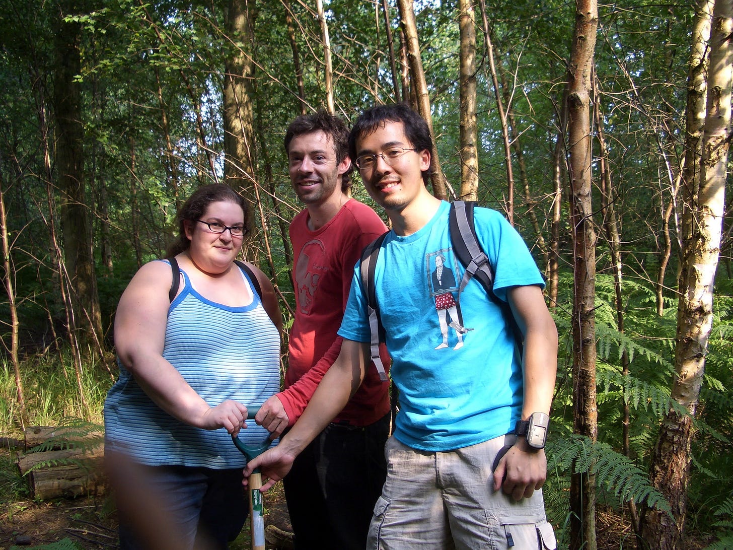 A woman and two men holding a shovel in a wood A woman and two men holding a shovel in a wood