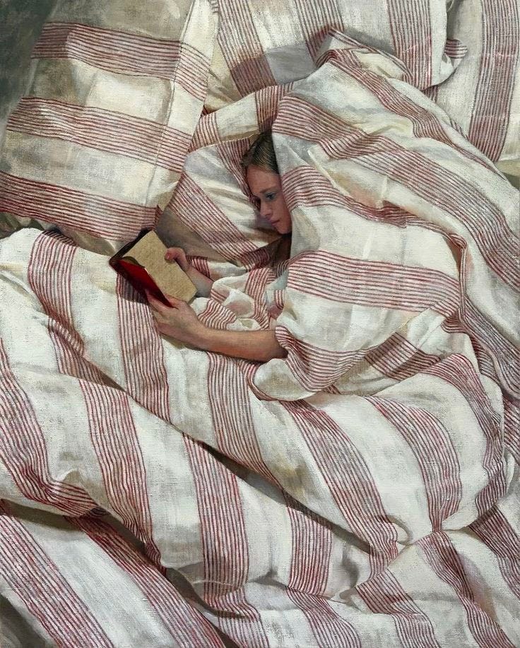 This may contain: a woman laying in bed under a blanket reading a book