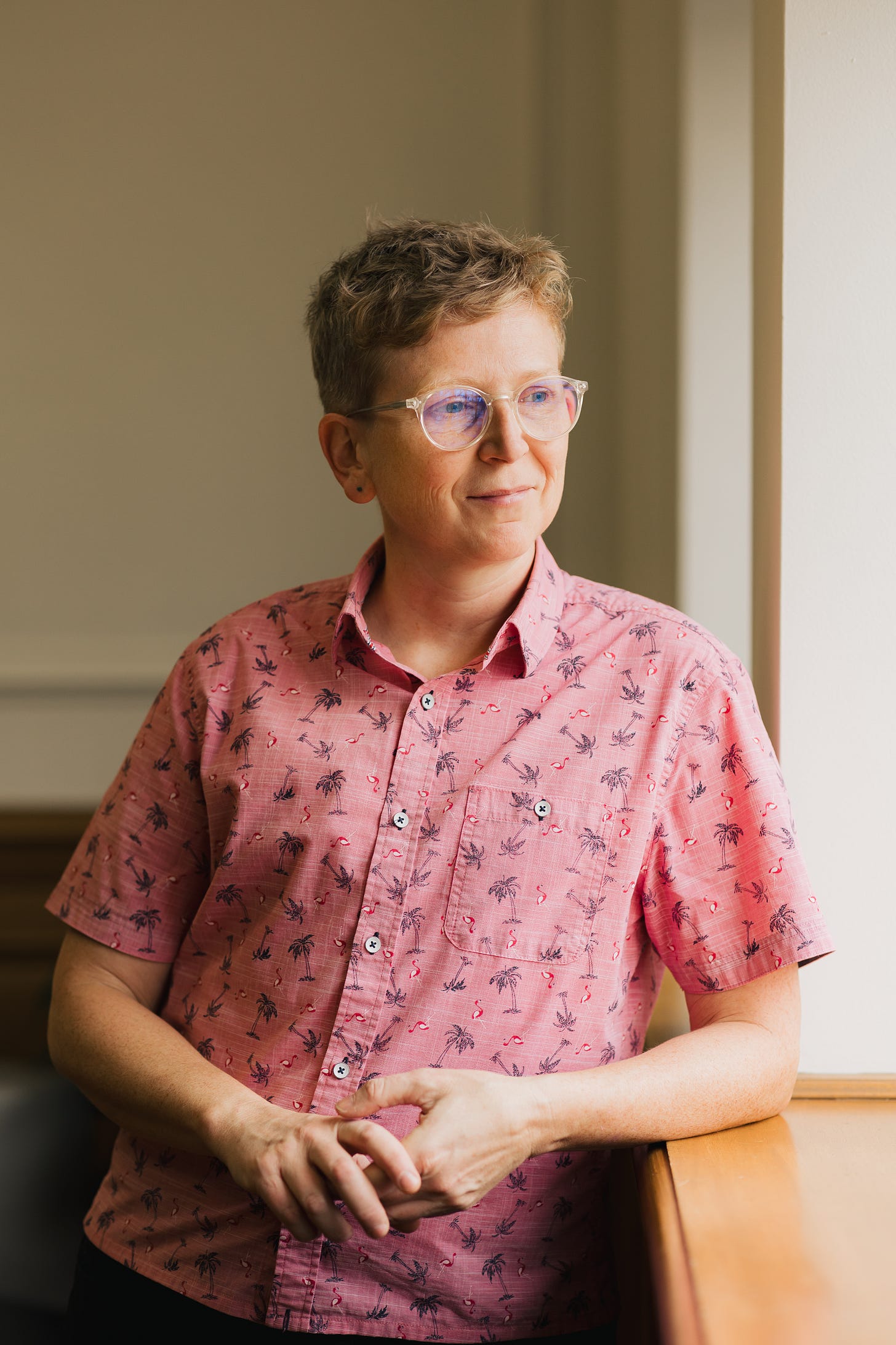 Laurie McGinley, looking out a window wearing a pink collared shirt