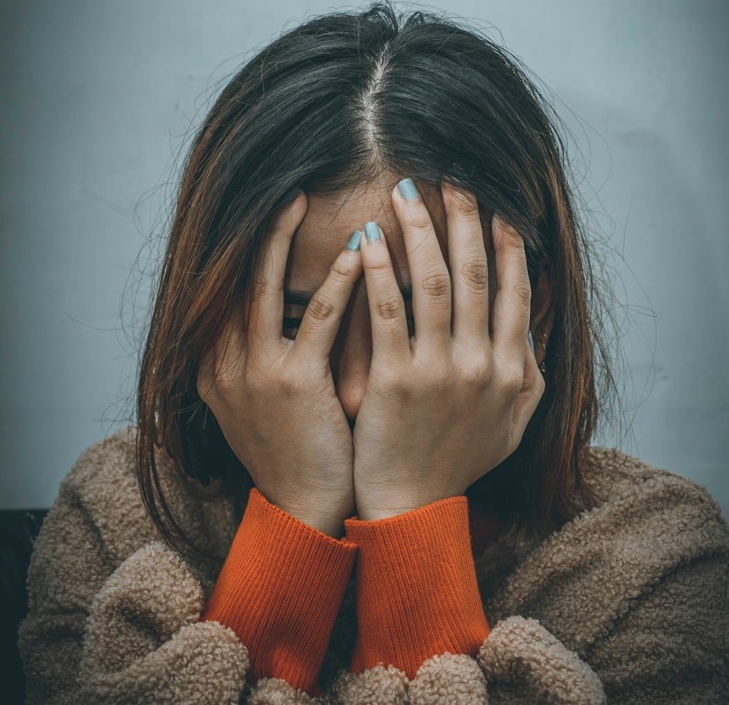 woman in brown sweater covering her face with her hand