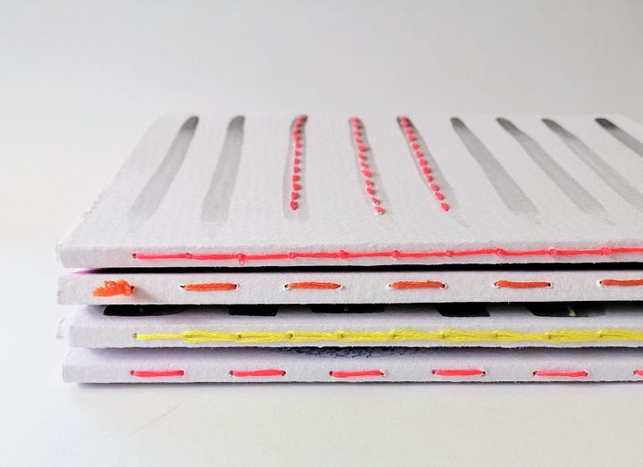 Four watercolour painted handmade notebooks with stitched details.