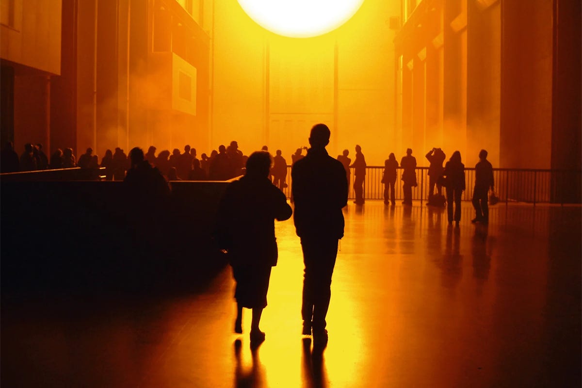 Visitors gather beneath the glowing artificial sun of Olafur Eliasson's "The Weather Project" inside Tate Modern's vast Turbine Hall.