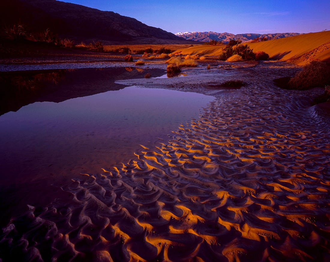 Ephemeral water reflecting dunes and mountains at sunset in Death Valley, with rippled sand glowing orange and purple Ephemeral water reflecting dunes and mountains at sunset in Death Valley, with rippled sand glowing orange and purple