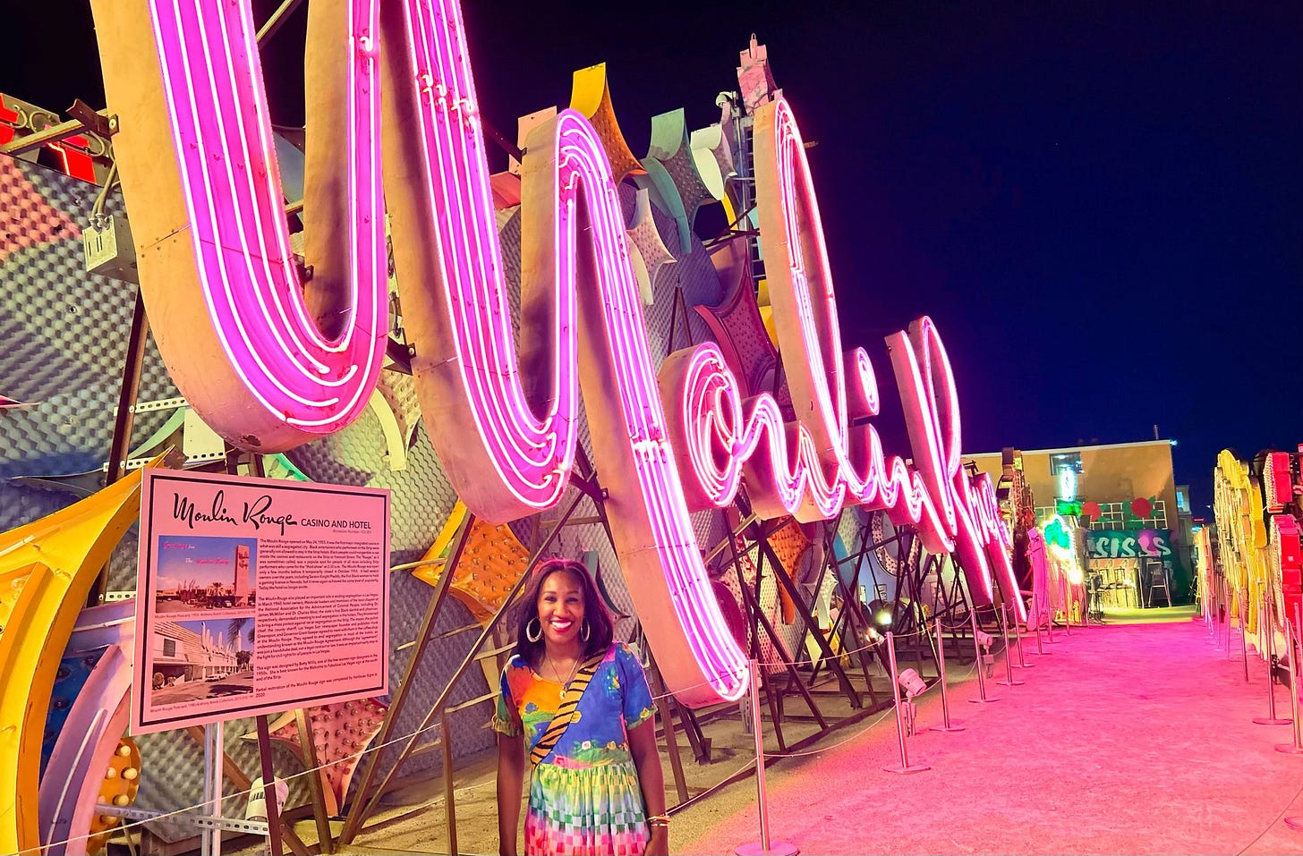 Shaunda Necole standing in front of the illuminated Moulin Rouge sign at the Neon Museum in Las Vegas, surrounded by vintage neon lights and historic casino signage. A vibrant nighttime scene representing Las Vegas history, culture, and community.