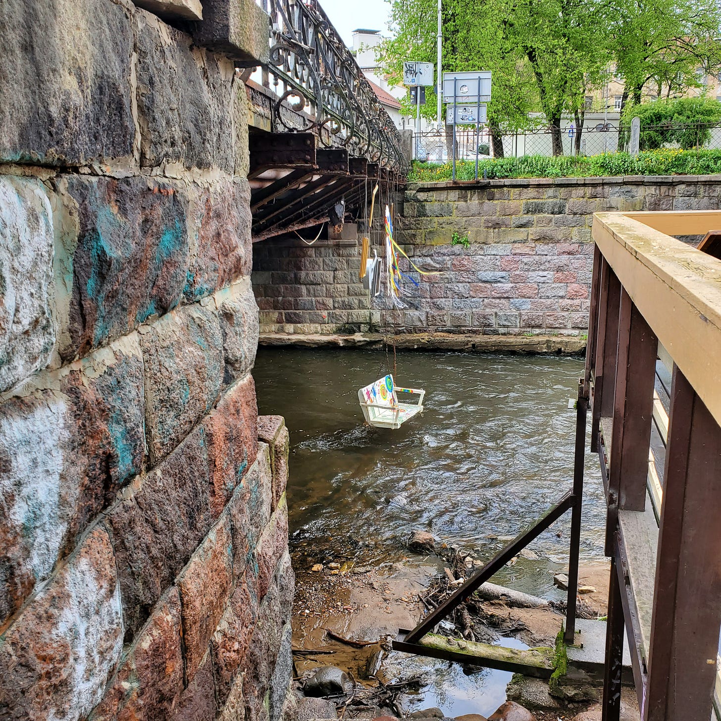 A brightly painted porch swing hangs from the bridge, over the river. 