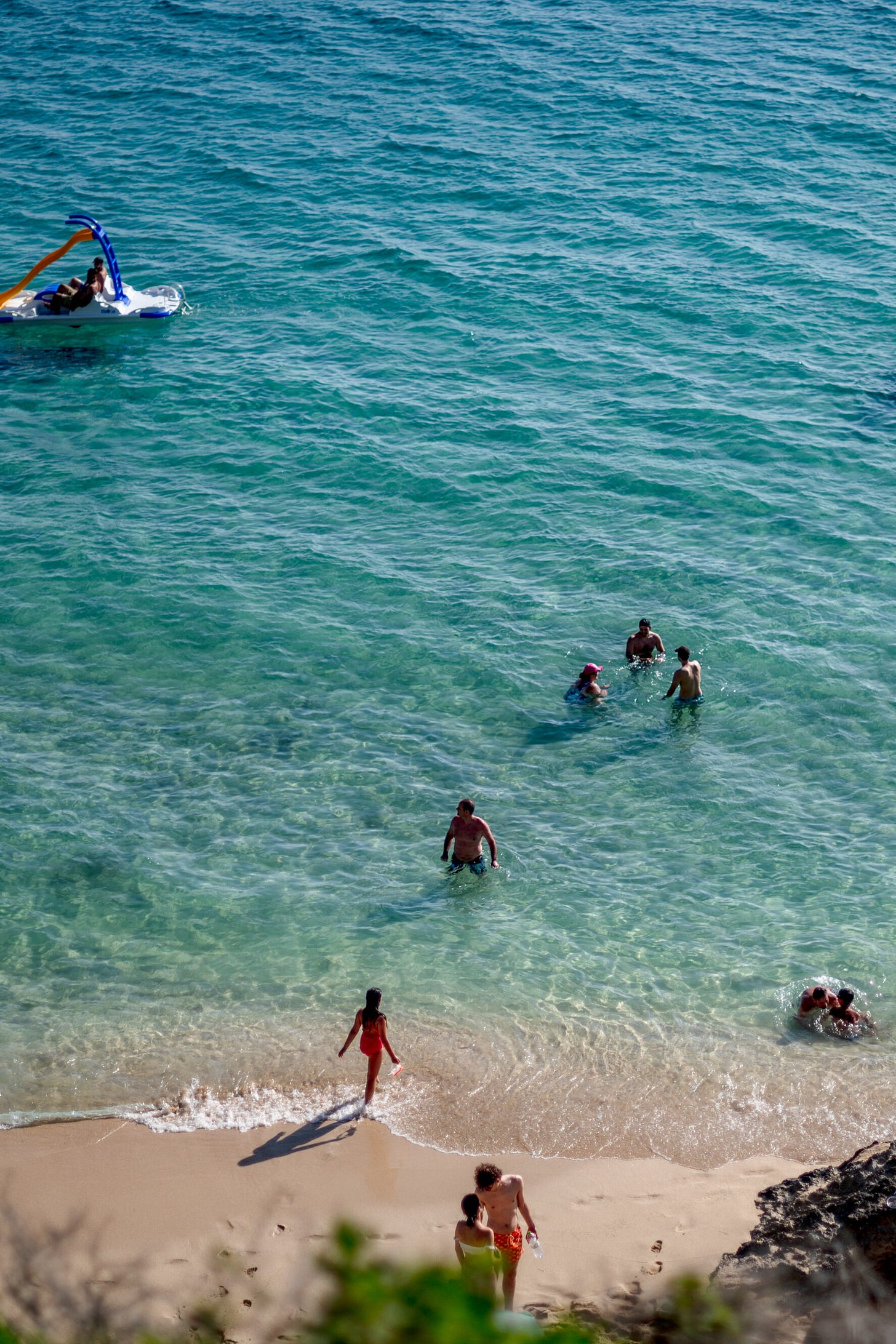 People frolic in the aquamarine waters on a beach.