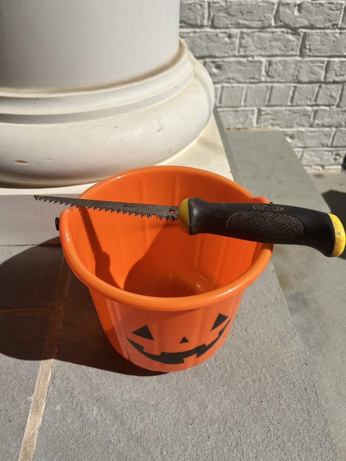 A drywall saw with a toothed blade resting on top of an uncarved orange pumpkin. A drywall saw with a toothed blade resting on top of an uncarved orange pumpkin.