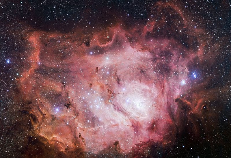 A celestial cloud of swirling gases, concentric pink ruffles containing patch of very bright stars. A celestial cloud of swirling gases, concentric pink ruffles containing patch of very bright stars.