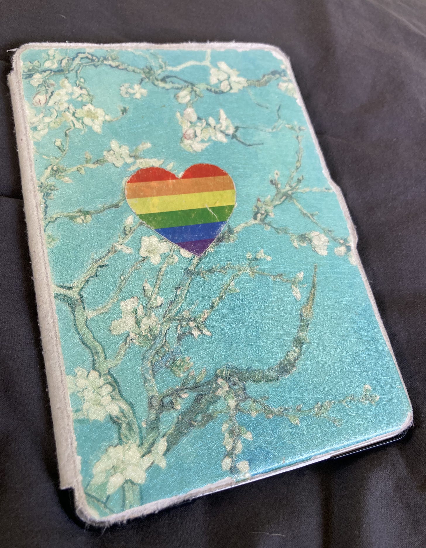 A light blue, faded Kindle cover with a rainbow heart sticker on the front. 