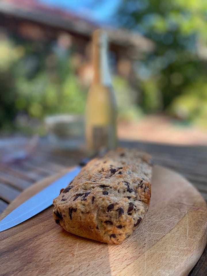 A glass of cava and a loaf of banana and chocolate bread on a wooden board