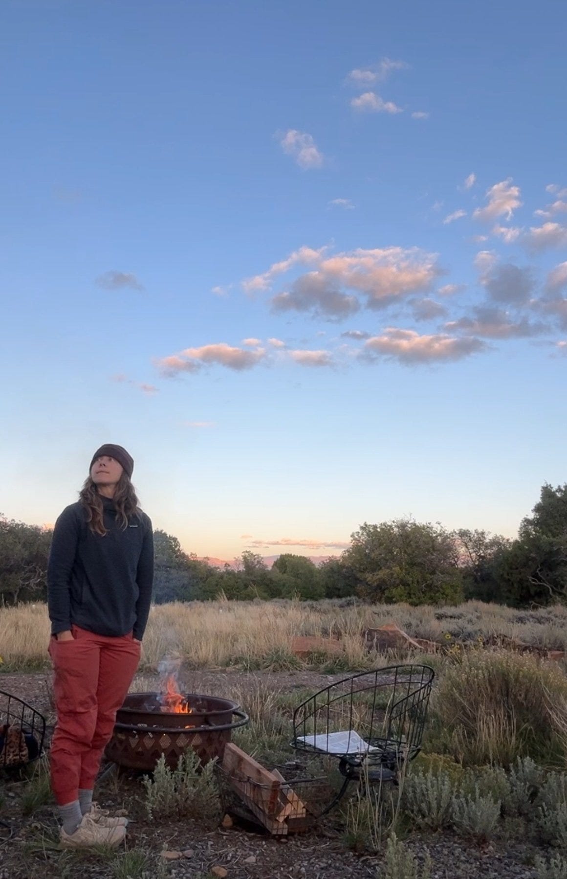 Woman standing over a bonfire with puffy clouds in the sky