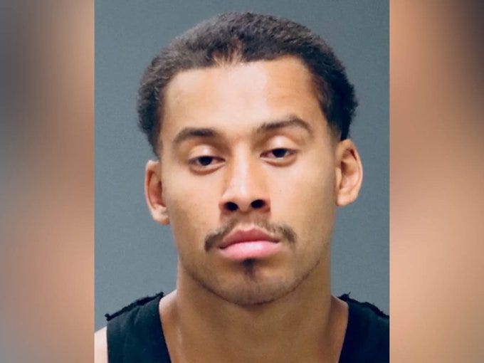 Mugshot of a young man with short hair and a mustache, displaying a serious expression against a neutral background.