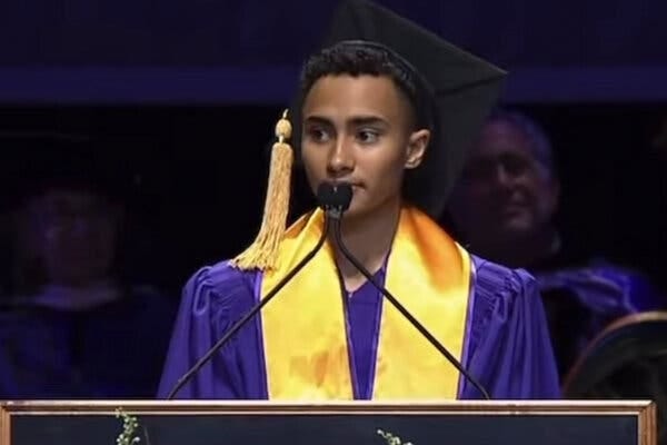Logan Rozos, a graduation speaker at New York University, wears a purple gown, a yellow sash and black mortar board with a yellow tassel.