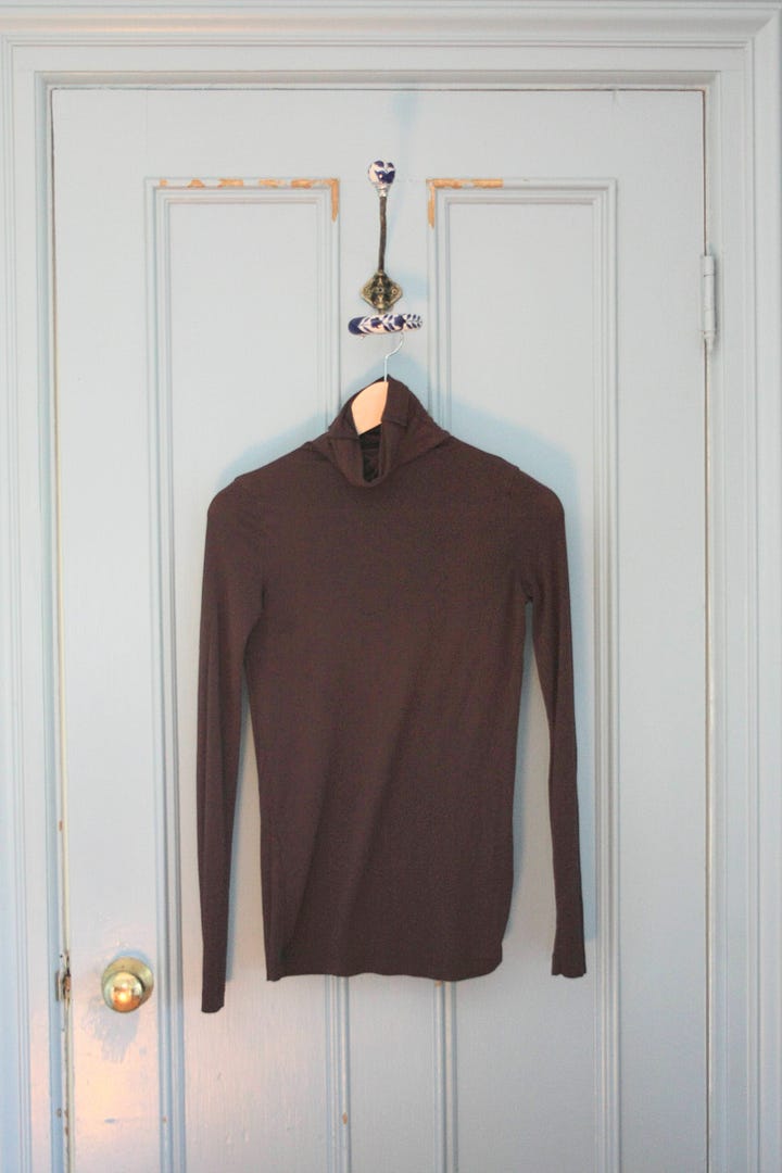 Five shirts, from left to right a white shirt, green turtleneck, oatmeal turtleneck, white t-shirt, and brown turtleneck