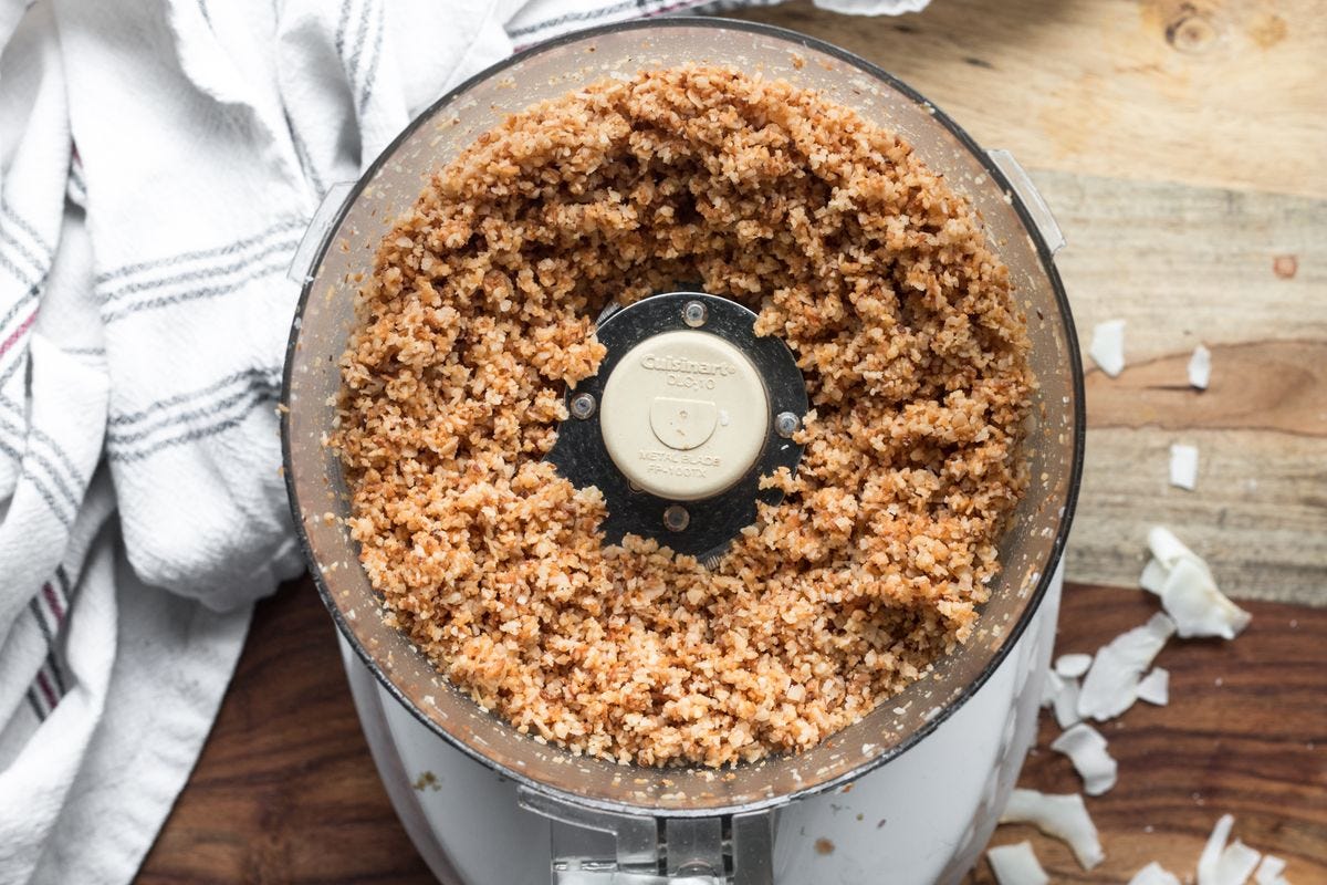 Overhead shot of food processor with coarsely ground coconut. White kitchen towel. Overhead shot of food processor with coarsely ground coconut. White kitchen towel.