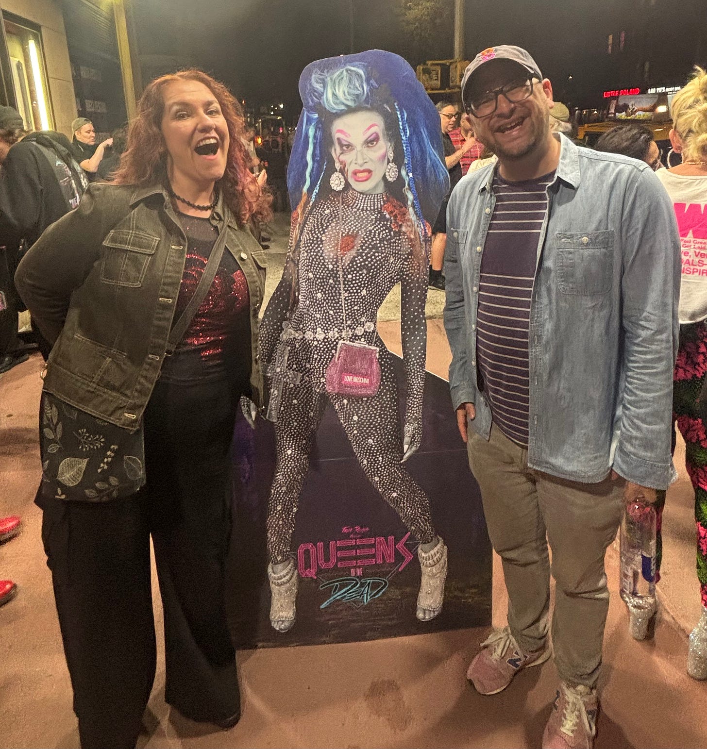 Me and Erin beside a "Queens of the Dead" cardboard cutout featuring a zombie drag queen. It's night and we're outside a movie theater in the east village.