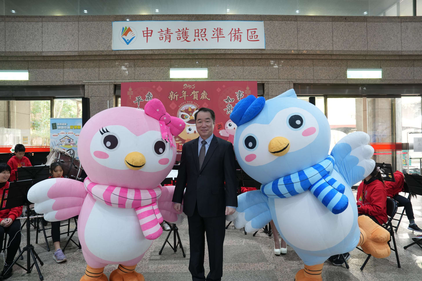 Caption 1: He Zhenhuan, Director of the Consular Affairs Bureau of the Ministry of Foreign Affairs, takes a photo with the mascots Bo Ge and Bo Mei.