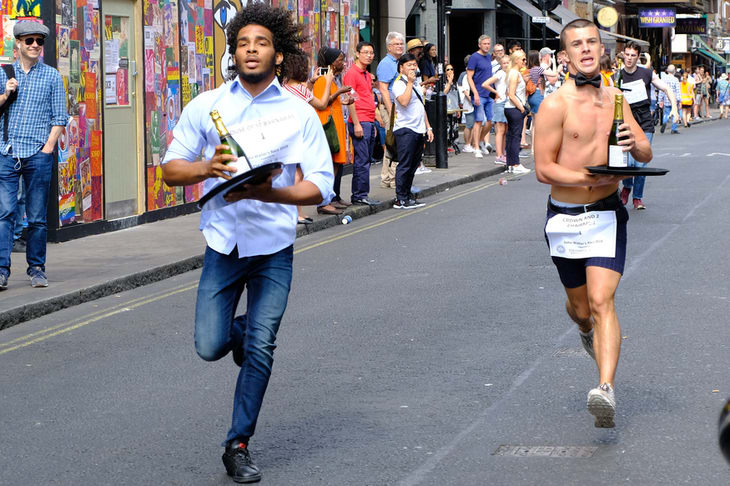 Two waiters running to the finish line - one is topless