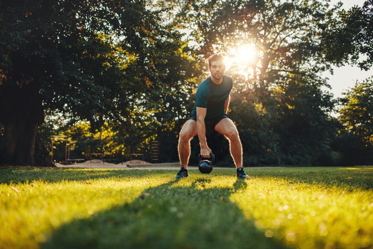 Full length portrait of healthy young man training with kettlebell in the park. 