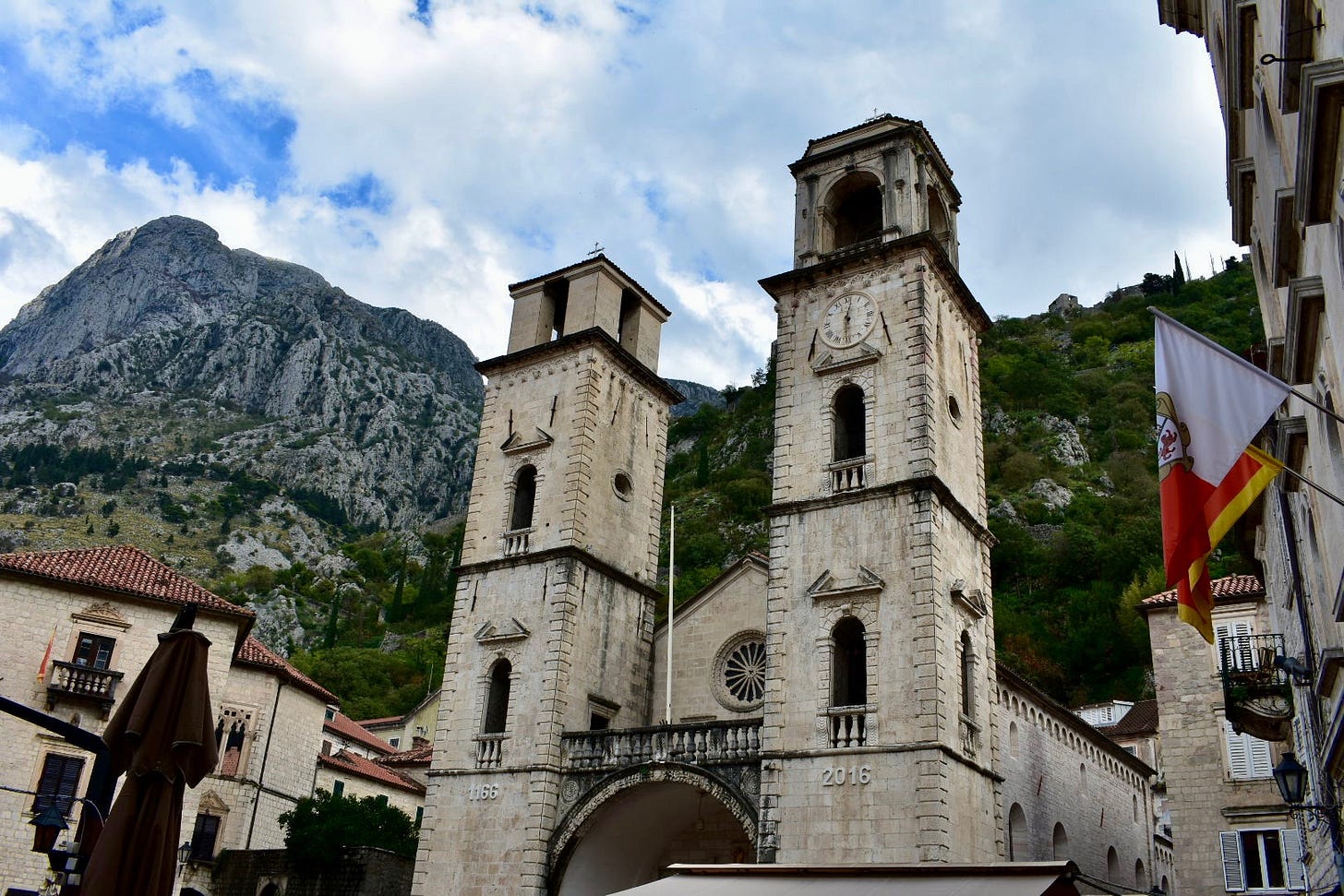 Medieval stone clock tower and cathedral facade in Kotor's UNESCO-listed Old Town, Montenegro, with limestone peaks rising sharply behind the city walls