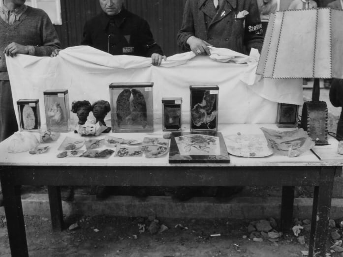 A group of men standing behind a table with objects on it

AI-generated content may be incorrect.