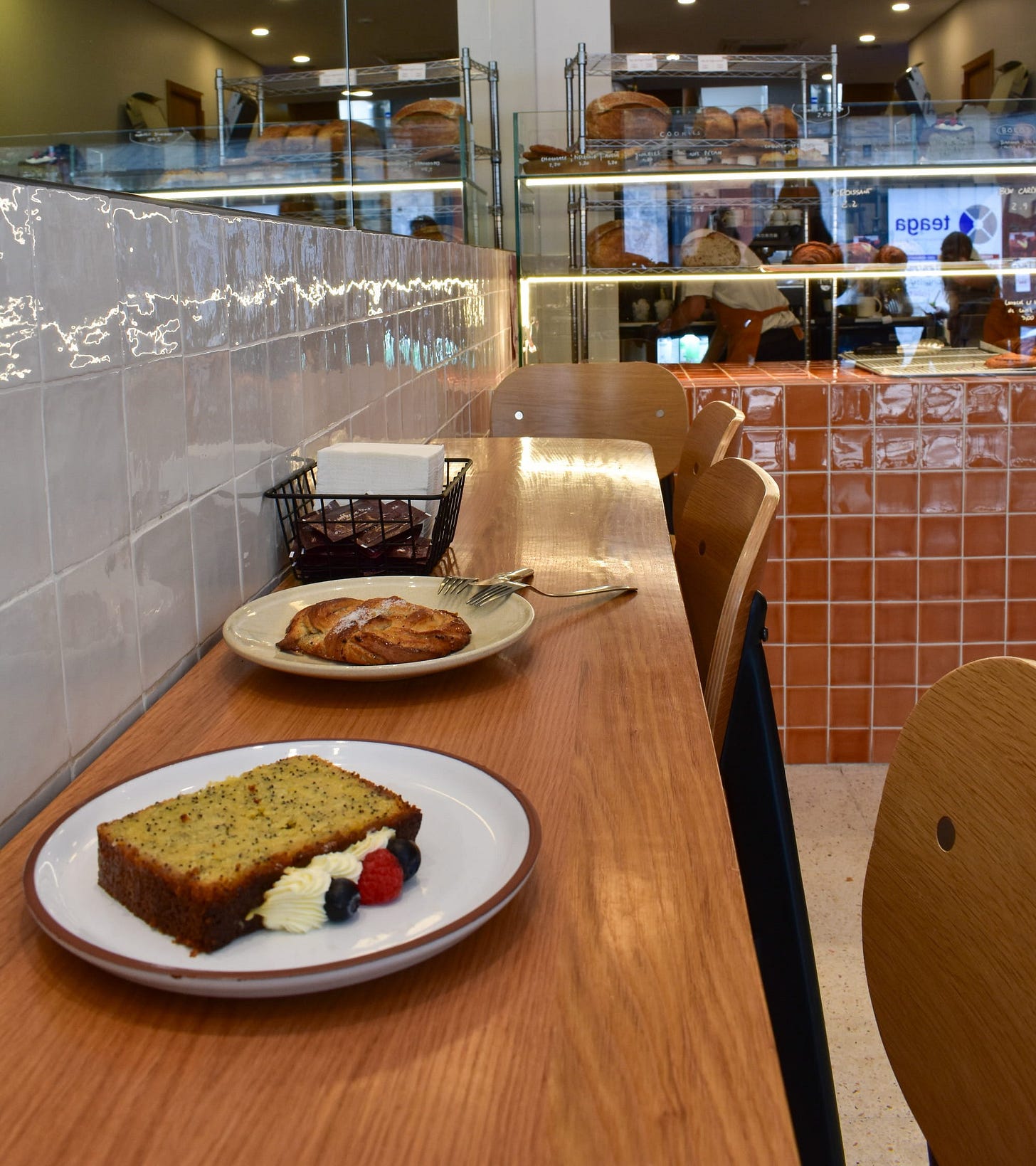 Lemon poppyseed loaf with whipped cream and berries alongside a pastry at MiBa Bakery in Porto, Portugal, with terracotta tiles and bakery cases in the background