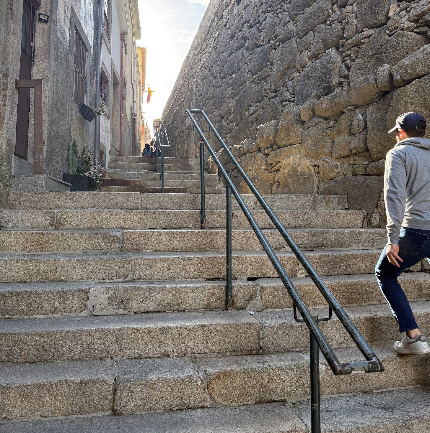A man walking up a steep, hidden, narrow side street in Porto, Portugal during golden hour.