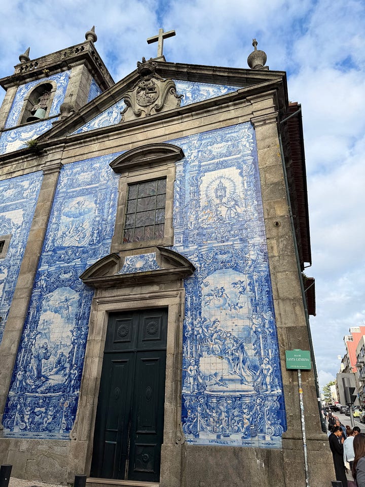 The blue and white azulejo tile facade of Igreja do Carmo church in Porto, Portugal, with baroque stone detailing and a tuk-tuk parked in the cobblestone square below