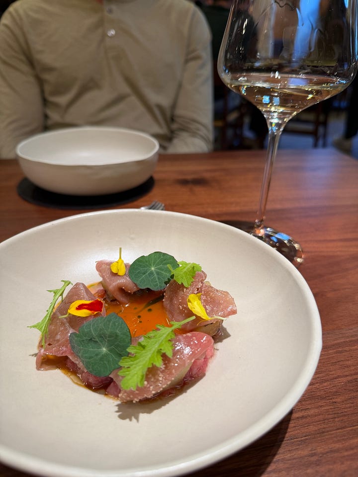 A delicate fish crudo dish with edible flowers, nasturtium leaves, and a glass of white wine at Cozinha das Flores restaurant in Porto, Portugal