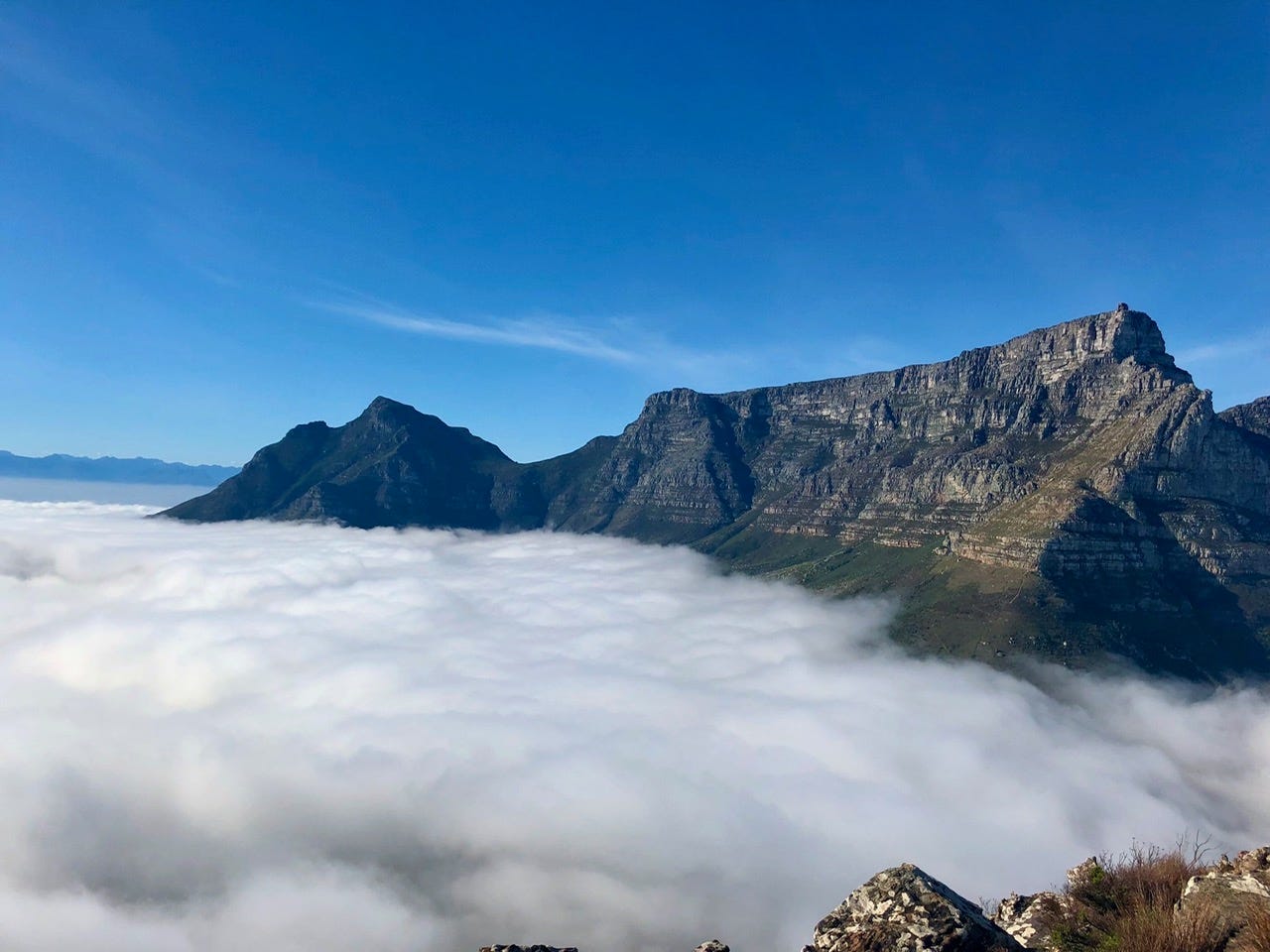 Table Mountain in Cape Town rising above a thick blanket of white cloud, the distinctive flat peak silhouetted against blue sky.