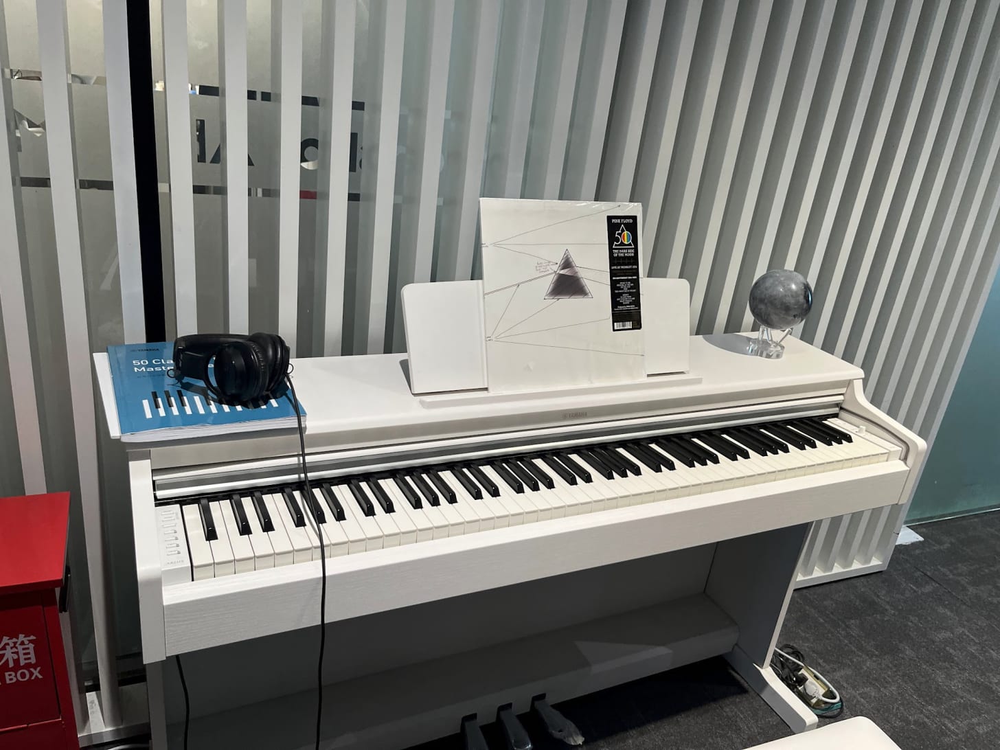A white Yamaha upright digital piano in the lobby of the Moonshot AI office, with a vinyl copy of Pink Floyd's "The Dark Side of the Moon" 50th anniversary edition displayed on the music stand.