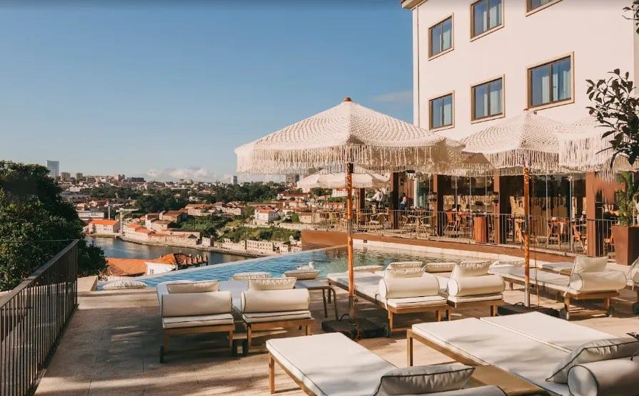 The outdoor pool terrace at Torel Avantgarde hotel in Porto with white sun loungers, fringed umbrellas, and panoramic views over the Douro River and Porto rooftops
