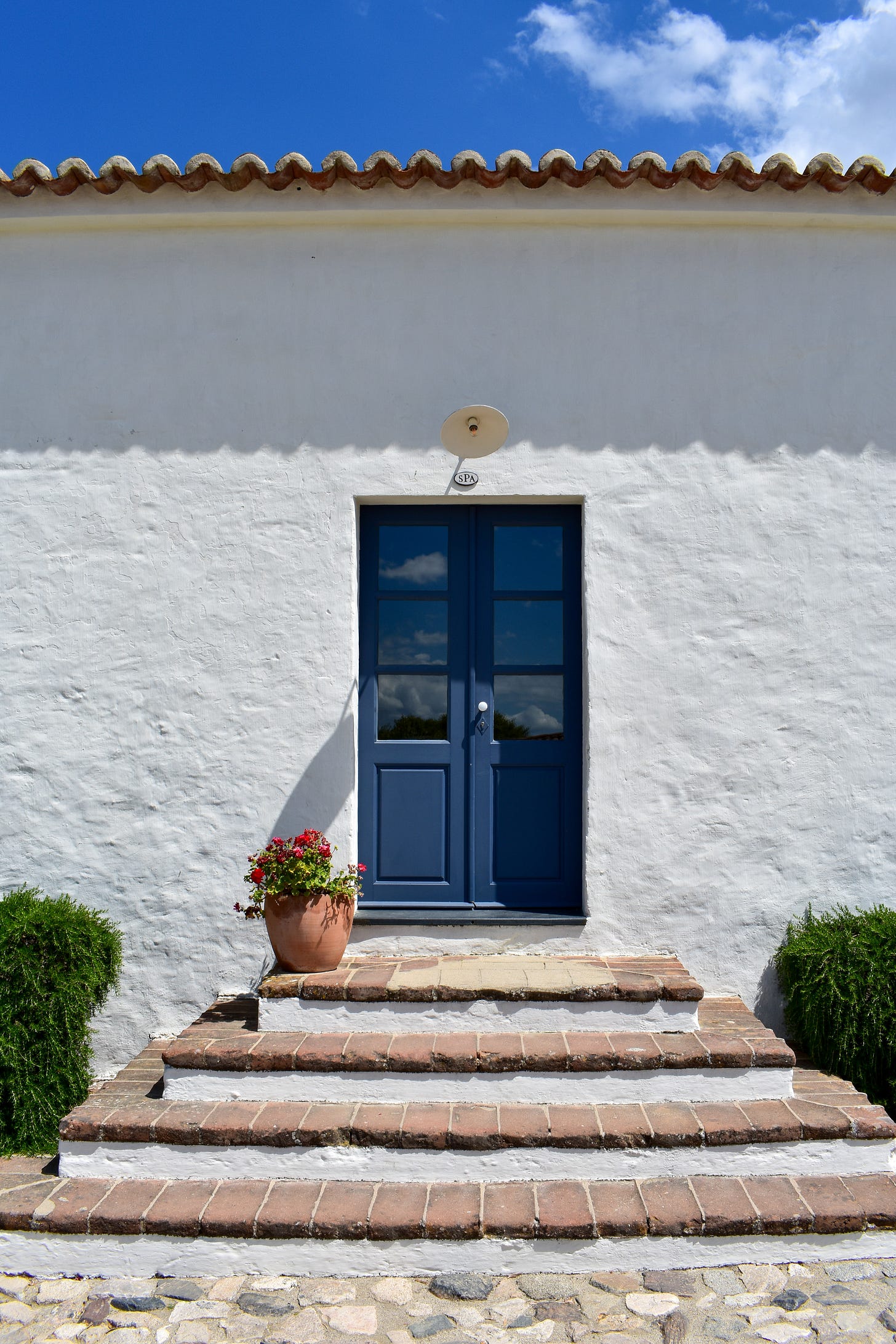 The spa entrance at São Lourenço do Barrocal — a blue double door on a whitewashed building with a SPA sign above and terracotta steps leading up